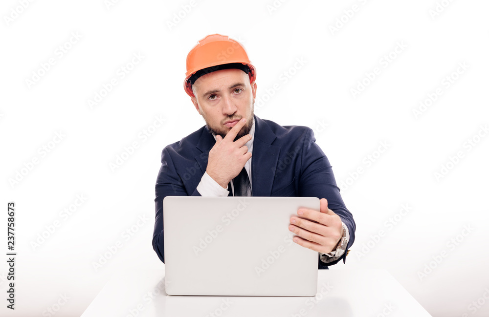 A tired constructor businessman in an orange helmet looks at the laptop screen and studies the construction project. Sits at the table and drinks coffee, nervous A tired constructor businessman in an orange helmet looks at the laptop screen and studies the construction project. Sits at the table and drinks coffee, nervous