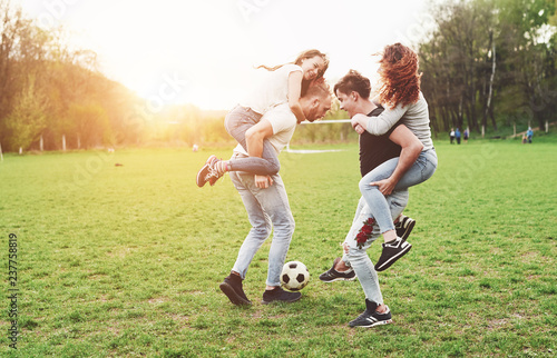 A group of friends in casual outfit play soccer in the open air. People have fun and have fun. Active rest and scenic sunset.