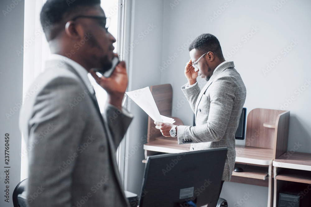Modern businessman at work. Two confident business people in formalwear discussing something While one of them looks at the documents and the second an important phone call Modern businessman at work. Two confident business people in formalwear discussing something While one of them looks at the documents and the second an important phone call