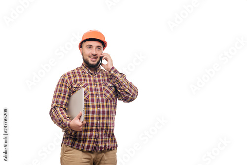 Happy Builder worker in protective construction orange helmet holding a laptop and talking on the phone, isolated on white background. Copy space for text. Time to work. 