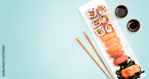 Sushi rolls set with salmon and tuna fish on light blue background from above.