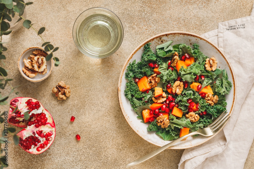 Top view on a vegetarian salad which is made from raw vegetables such a persimmon, kale, pomegranate seeds and walnut. Healthy food and lifestyle concept, flat lay.