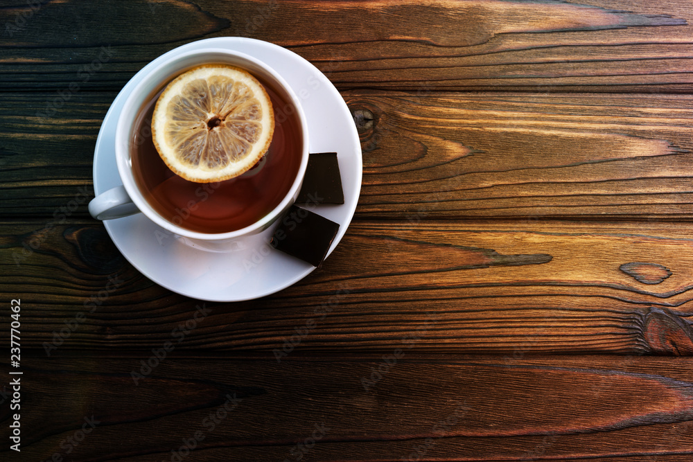 Obraz premium a Cup of tea with lemon, two pieces of chocolate on a wooden background. tea, drink, rest.