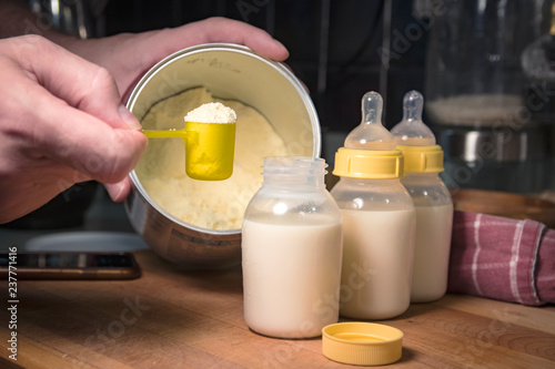 Photography Hand holding scoop of powdered baby formula, ready to mix in bottles