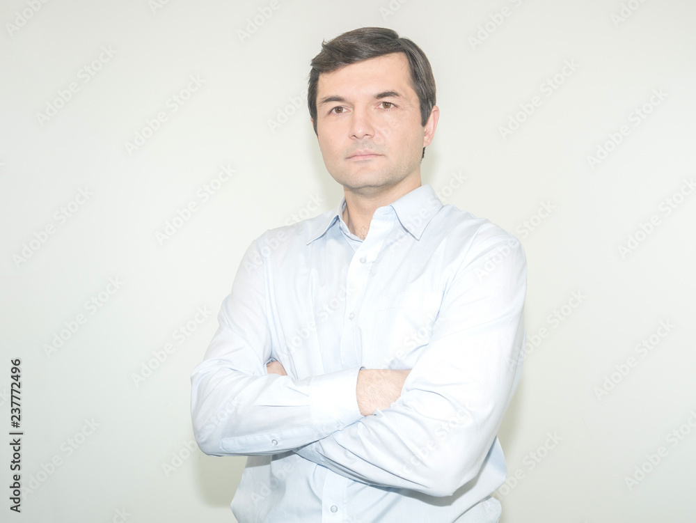 Serious man with arms folded standing isolated on a grey background and looking at camera Serious man with arms folded standing isolated on a grey background and looking at camera