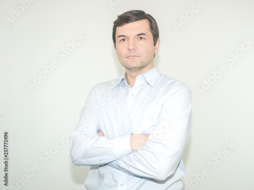 Serious man with arms folded standing isolated on a grey background and looking at camera © COK House