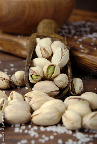 Salted pistachios in a scoop on a wooden background.