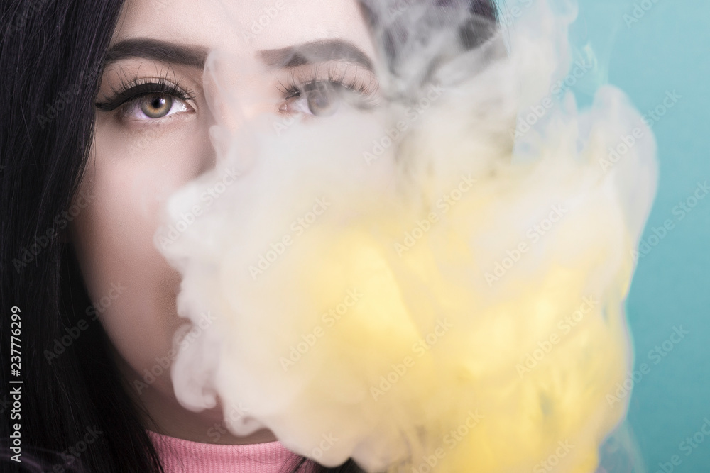 portrait of a woman who smokes an electronic cigarette and releases smoke from his mouth on azure background