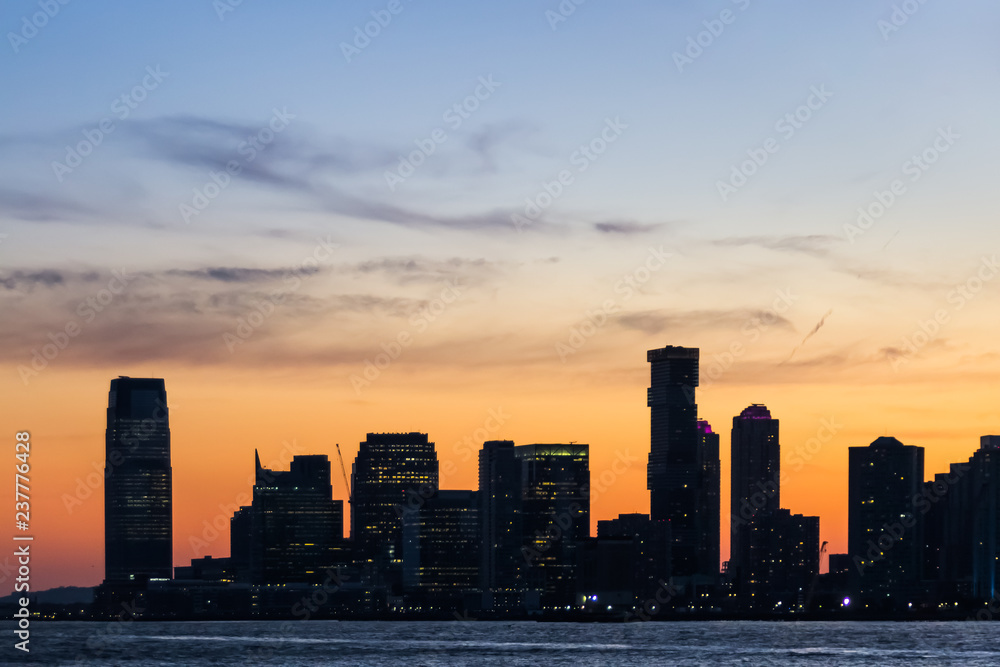 Night view over the Hudson River of the Jersey City skyline with colorful sky in the background