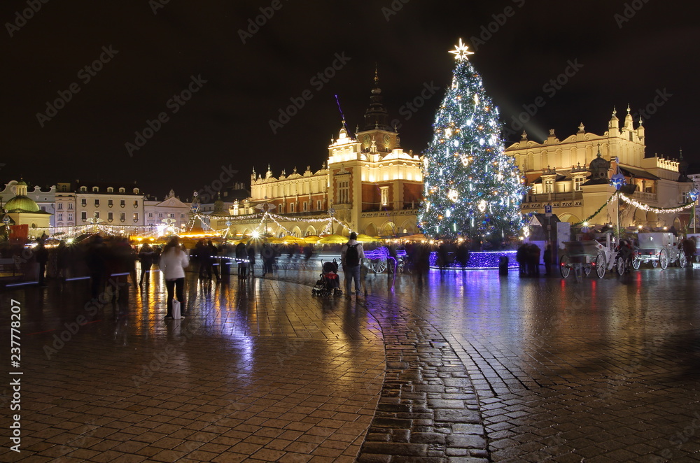 Krakow city center, Poland, main square at night decorated with beautiful huge Christams tree, buildings illuminated, nice reflections on wet ground