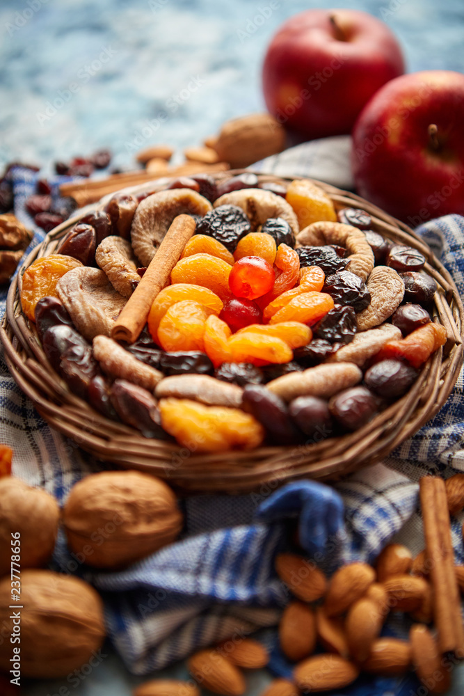 Composition of dried fruits and nuts in small wicker bowl placed on a stone table. Assortment contais almonds, walnuts, apricots, plums, figs, dates, cherries, peaches. Above view with copy space. Composition of dried fruits and nuts in small wicker bowl placed on a stone table. Assortment contais almonds, walnuts, apricots, plums, figs, dates, cherries, peaches. Above view with copy space.