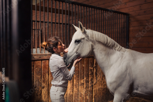 Girl jockey preparing her horse for riding in the stable photo