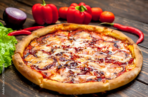 pizza on wooden table with ingredients, tomatoes, pepper, onion