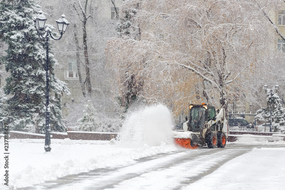 City service cleaning snow , a small tractor with a rotating brush clears a road in the city park from the fresh fallen snow on winter day City service cleaning snow , a small tractor with a rotating brush clears a road in the city park from the fresh fallen snow on winter day
