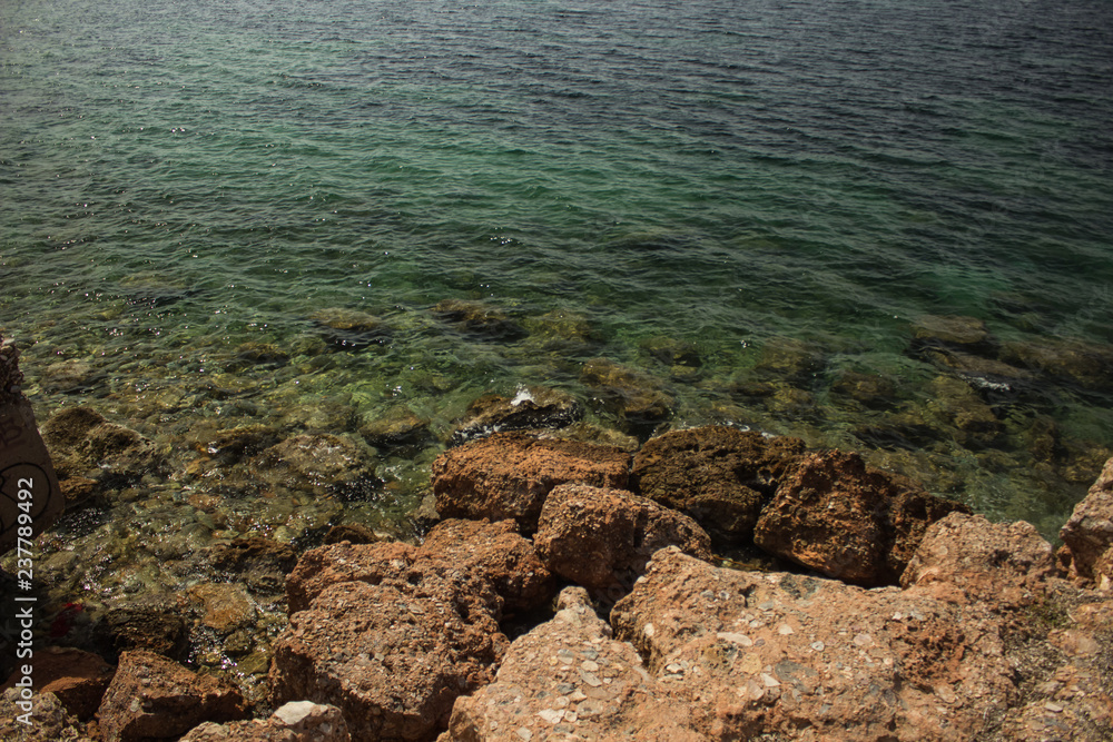 rock sea shore waterfront line with underwater stones in transparent green water surface Mediterranean landscape