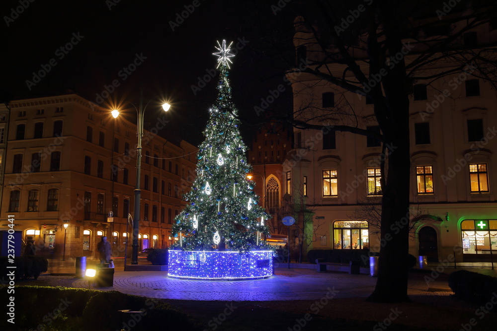 Big illuminated Christmas tree on square in Krakow city center, poland, at nioght, street lamps, lights, buildings