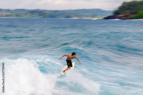Young man riding a surfboard in a blue wave in the summer.
