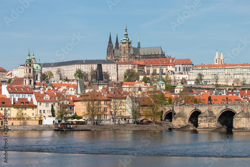 View of Prague Castle, Charles bridge and Vltava river. Beautiful Prague cityscape with classic red roofs and famous gothic church St. Vitus Cathedral and Baroque Church of St Nicholas.
