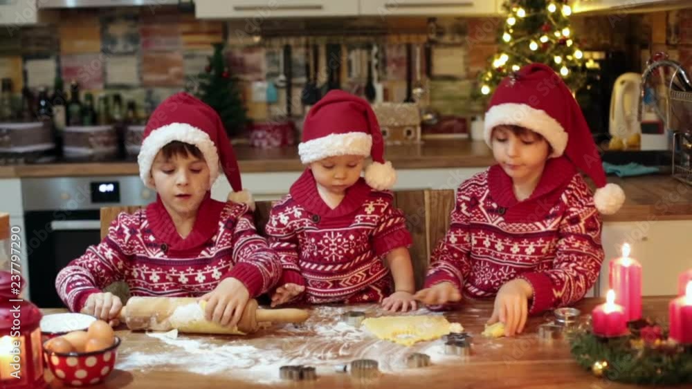 Sweet toddler child and his older brother, boys, helping mommy preparing Christmas cookies at home in kitchen Sweet toddler child and his older brother, boys, helping mommy preparing Christmas cookies at home in kitchen