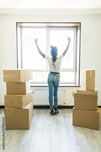 Rear view of Joyful young afro american woman standing in new apartment with arm raised after moving © F8  \ Suport Ukraine
