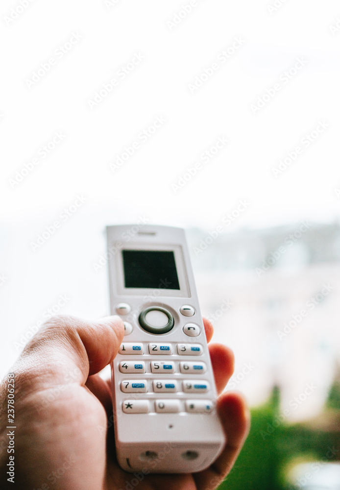Male hand holding outdoor home office white cordless phone dialing a number on the white keyboard - shallow dof Male hand holding outdoor home office white cordless phone dialing a number on the white keyboard - shallow dof