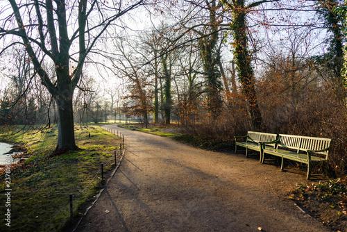 Outdoor sunny tranquil scenery landscape of empty benches no people along walkway on waterside of frozen canal or lake at Park Sanssouci in winter season in Potsdam, Germany.