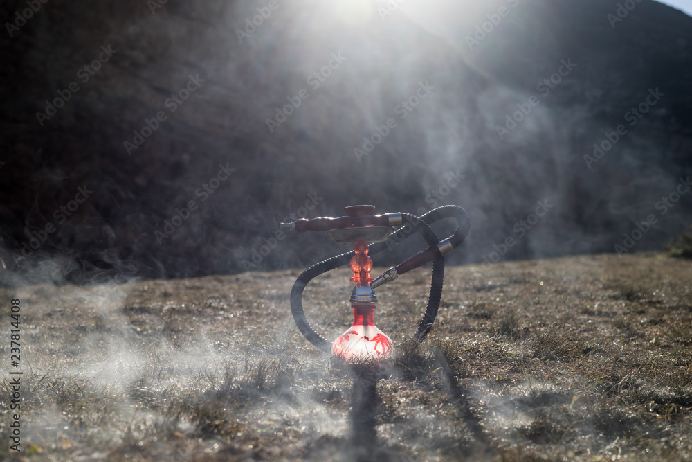 Obraz premium Hookah, traditional arabic waterpipe, direct sunset light, outdoor photo. Mountain background or Silhouettes of hookah on sunset background. Outdoor. Selective focus