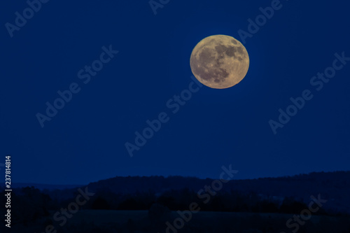 Full Moon over rolling hills silhouette with blue sky