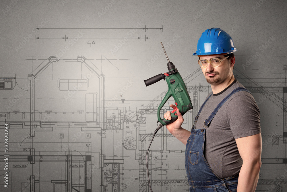 Worker standing with tool in his hand in front of technical drawings.
