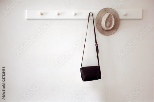 Foto Stylish hat and small black purse hanging on white pegs on wall in cozy room