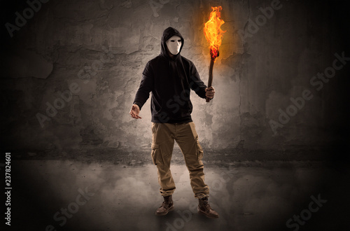 Ugly wayfarer with burning torch in his hand in front of a crumbly wall concept 