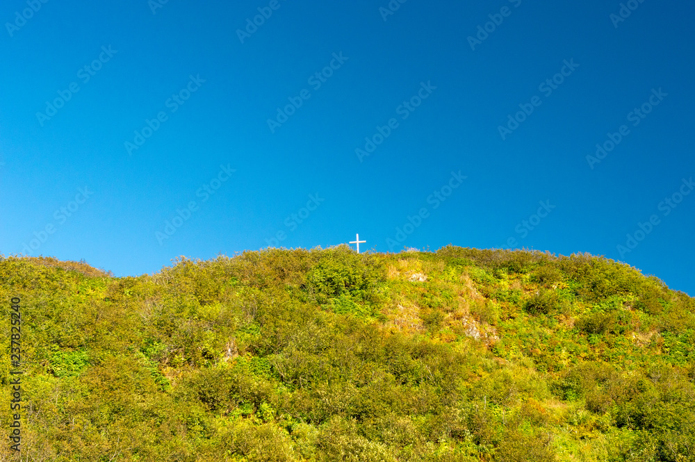 Tiny white cross on a large mountain peak against a clear blue sky.