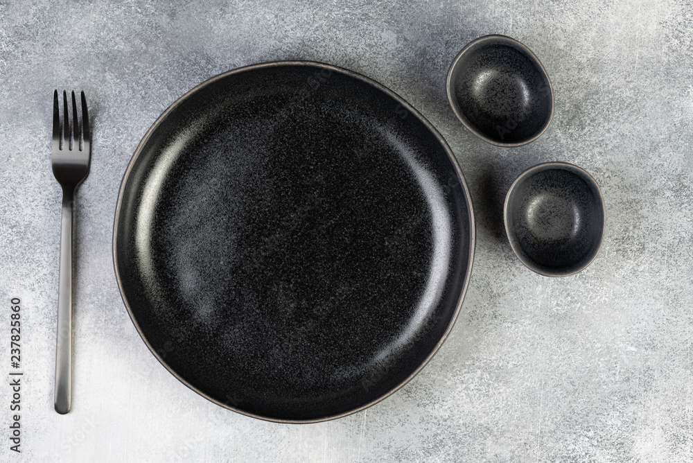 Empty black plate, fork, knife, spoon on blue background, top view