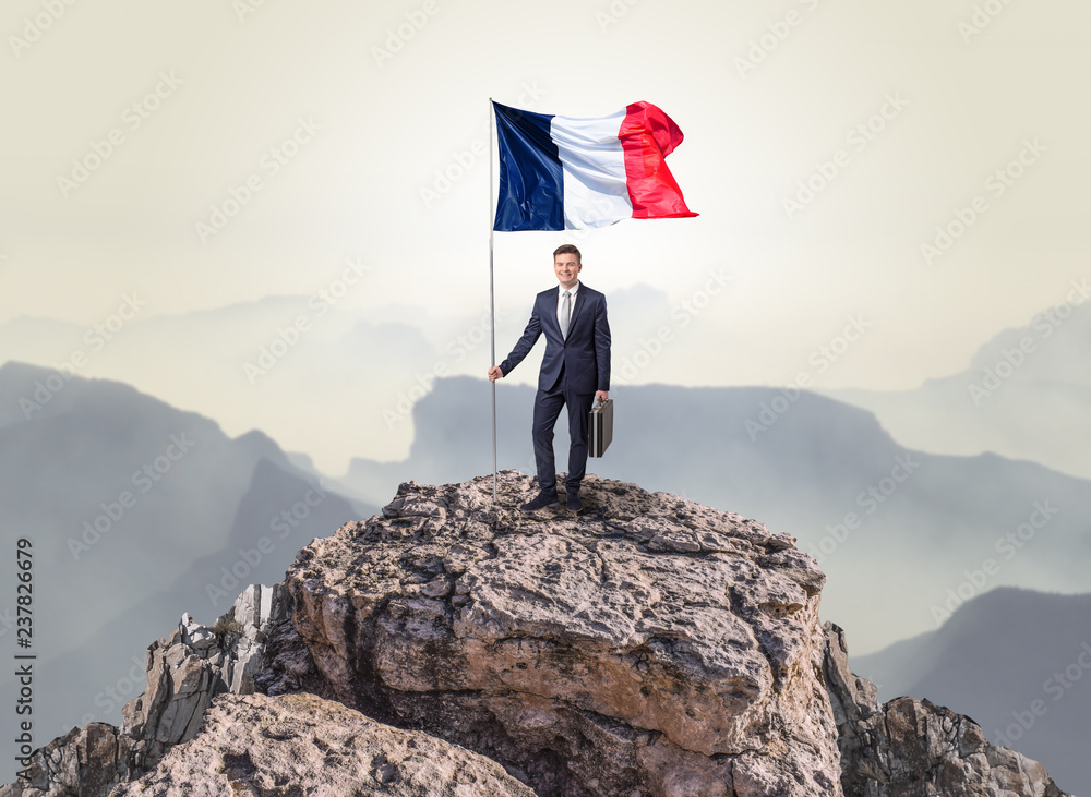 Obraz premium Successful businessman on the top of a mountain holding France victory flag 