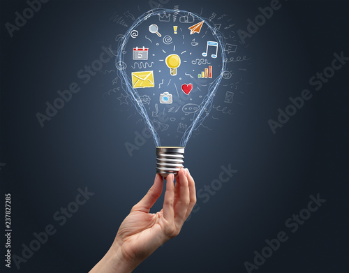 Hand holding light bulb on dark background. New apps concept