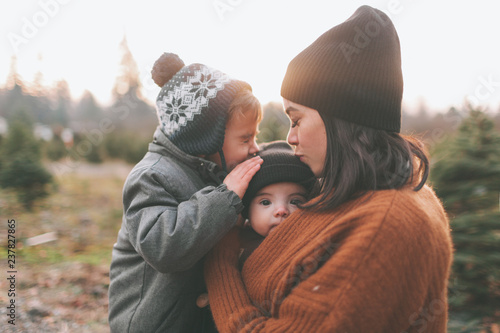 A mother and her son kissing a baby in winter.