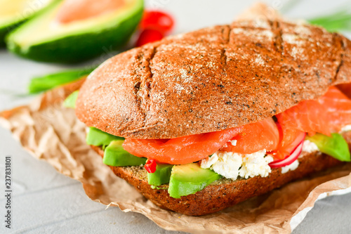 sandwich with avocado and salmon on a light background, green onions and gluten-free grain bread, radishes and tomatoes. concept diet food, copy space, sandwich take away, healthy fast food