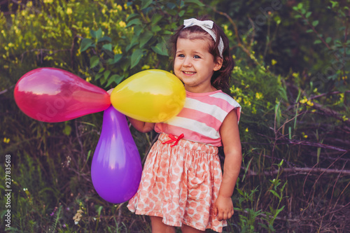 A little girl 3, 4 years old in a pink white dress is happy and laughs and holds balloons photo