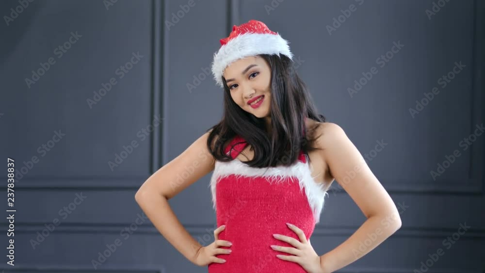 Portrait of beautiful Asian woman wearing Santa Claus hat and suit smiling and posing at studio