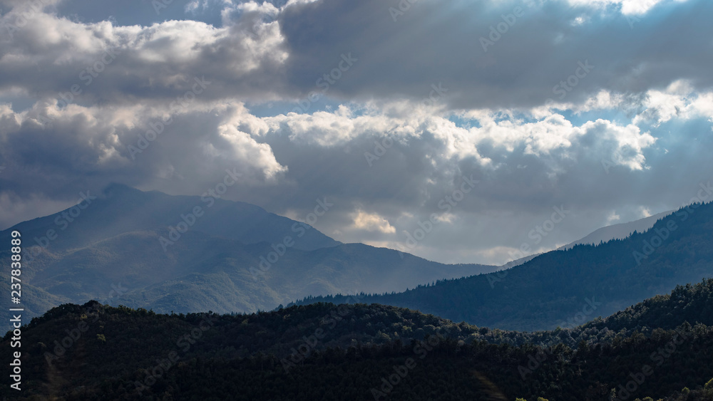 Sun rays thru cloudscape lighting mountain peak forest in Catalonia