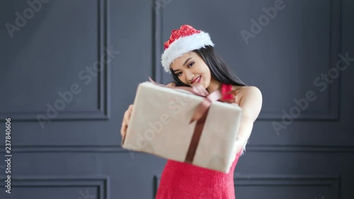 Adorable female Santa Claus gives big gift box in Christmas time at studio medium shot