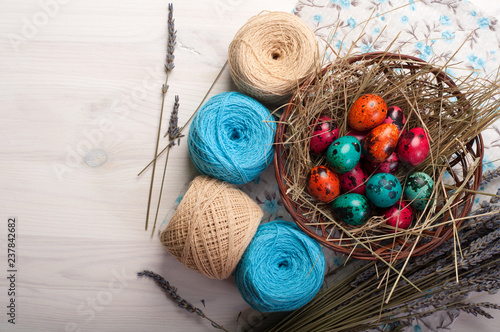 Easter background. Multicolored eggs in a basket, flowers, tangles of thread and decoration on a white wooden background. Space for text (free space) photo