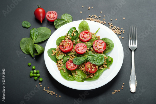 Salad of baby spinach leaves, green lentils, cherry tomatoes, olive oil and lemon juice in a bowl on a dark surface. A dietary dish. Vegetarian, vegan concept