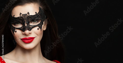 Happy woman in carnival mask. Fashion model with red lips makeup on black background with copy space