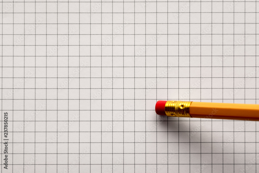 Erased of yellow pencil on a sheet of light gray squared paper. Tilted side view Erased of yellow pencil on a sheet of light gray squared paper. Tilted side view