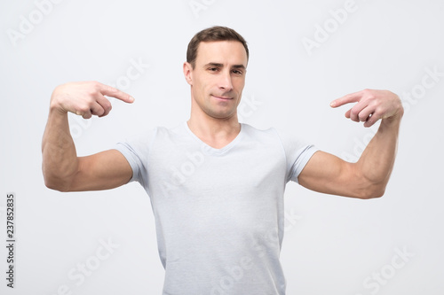 Italian man in white t-shirt, standing, pointing himself and looking with serious egoist face. photo
