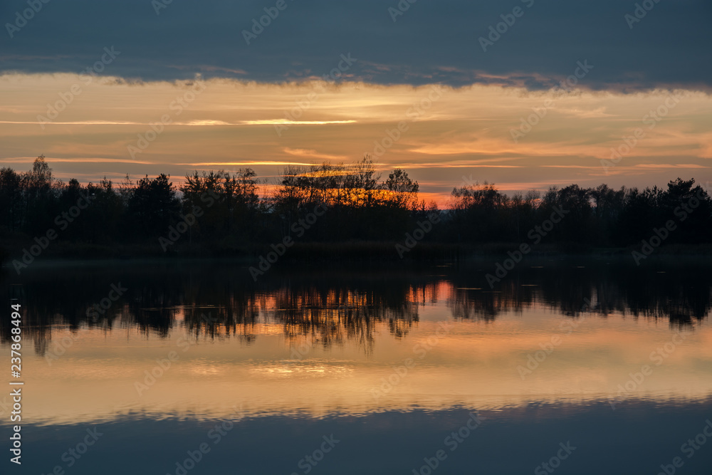 Trees on the shore of the lake and reflection of clouds after sunset