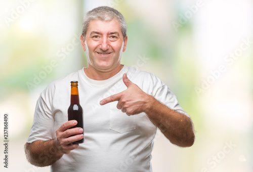 Handsome senior man drinking beer bottle over isolated background very happy pointing with hand and finger