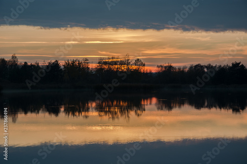 Trees on the shore of the lake and reflection of clouds after sunset