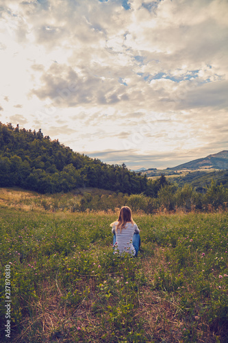 Girl sitting on a green meadow and watching the countryside landscape.